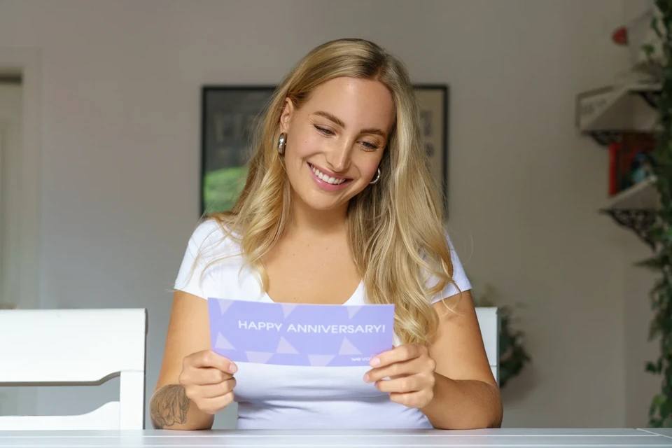 Eine Frau liest lächelnd eine Happy-Anniversary-Grußkarte von thevalyoubox.